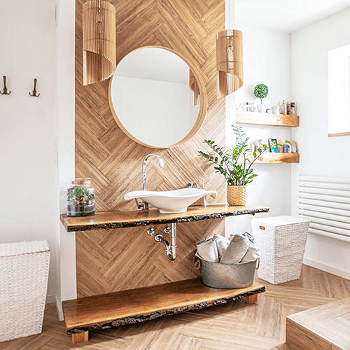 Ein Badezimmer mit Parkett-Boden und Holzdetails an der Wand. Im Fokus steht ein freistehendes Waschbecken und ein runder Spiegel.