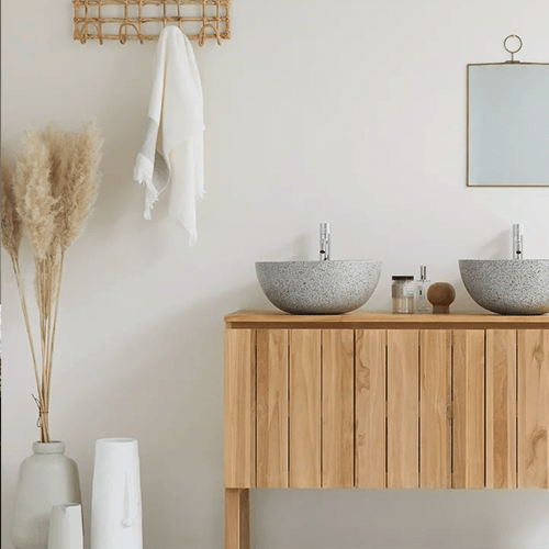 Ein Badezimmer mit Doppelwaschbecken, Unterschrank, Vasen mit Pampas-Gras und einen kleinen Wandspiegel.