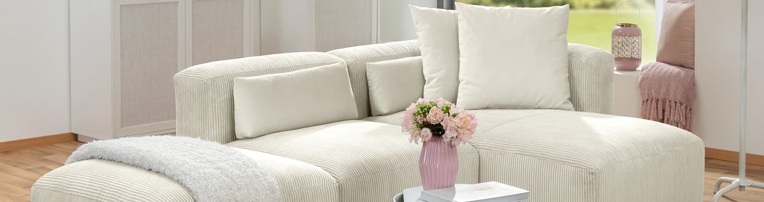 Ecksofa aus Cordstoff in beige in einem Wohnzimmer mit hellen Möbeln und Dekoration in rosa