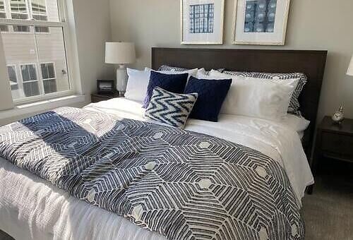 Ordentlich gemachtes Bett mit dunkelblau gemusterter Tagesdecke